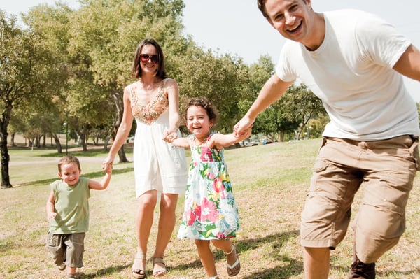 Family holding hands and running through a park