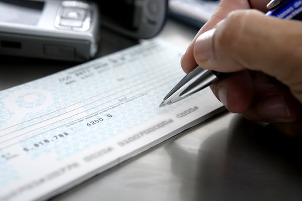 A hand holding a pen, filling out a check