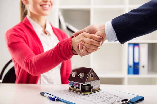 A man and woman shaking hands over a model house in a concluded business deal