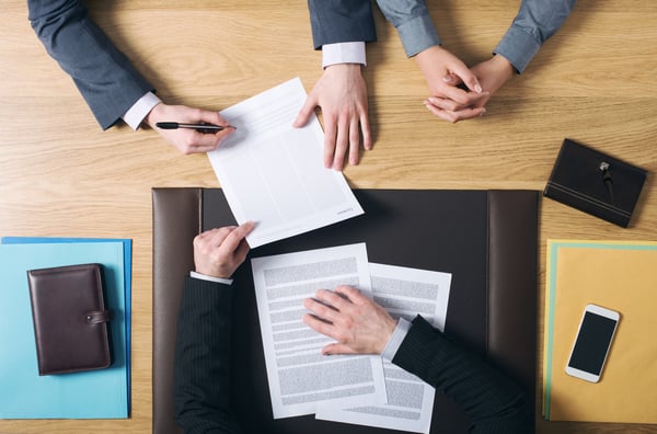 Top down view of a business meeting with three people discussing a document before signing